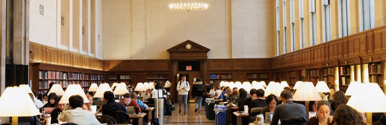 Students fill the tables in the vast main reading room of Columbia University's Butler Library where light pours in from the tall windows and the central chandelier.